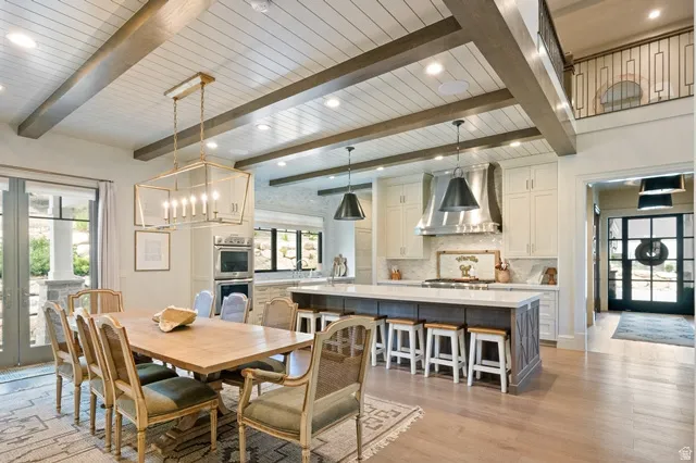 Open-concept interior featuring wood-finish flooring, a shiplap ceiling with exposed beams, a kitchen island with seating, a built-in oven, and a balcony with an iron railing