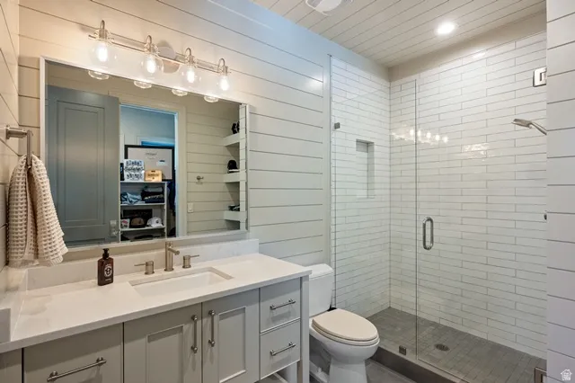 Contemporary bathroom featuring a spacious glass-enclosed shower with subway tile surround, single vanity with integrated sink and stone countertop, shiplap wall finishes, and brushed nickel hardware
