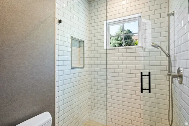 Shower enclosure featuring subway tile surround, clear glass paneling, built-in shower niche, brushed nickel showerhead and fixtures, and a high-set window