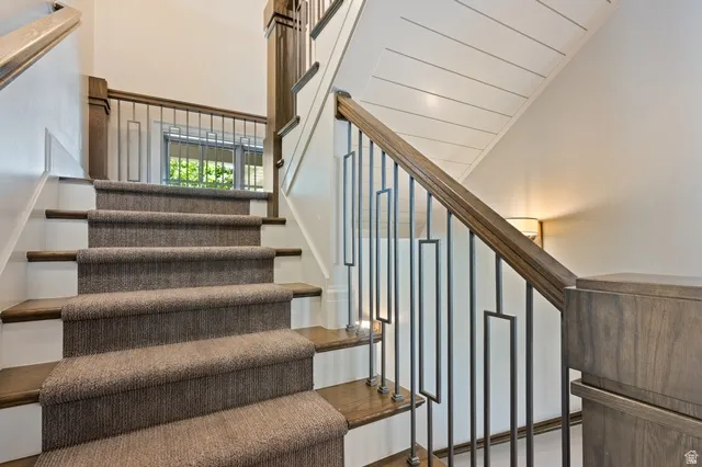 Staircase featuring wood-finish treads, a carpet runner, and a custom wrought iron railing with wood-finish handrail and newel posts