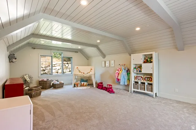 Spacious room featuring a vaulted ceiling with exposed beams, recessed lighting, and light-colored carpeting
