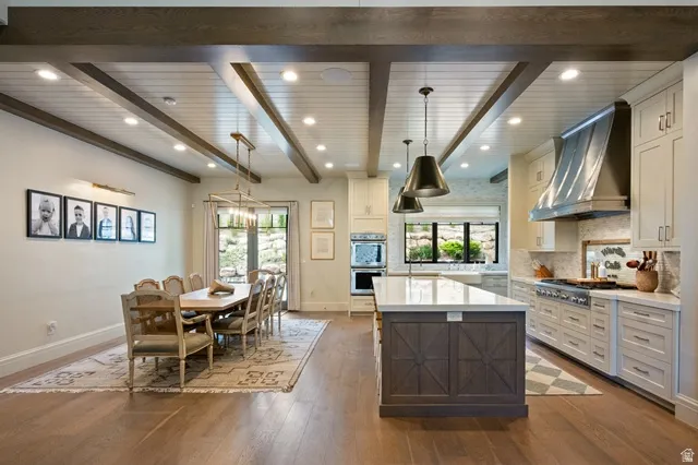 Open-concept living space featuring wood-finish flooring, a coffered ceiling with recessed lighting and exposed beams, and a dining area with a brass chandelier