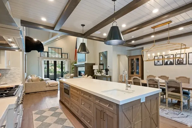 Open-concept living space featuring a spacious kitchen island with integrated sink, wood-finish flooring, exposed ceiling beams, and a fireplace in the living area