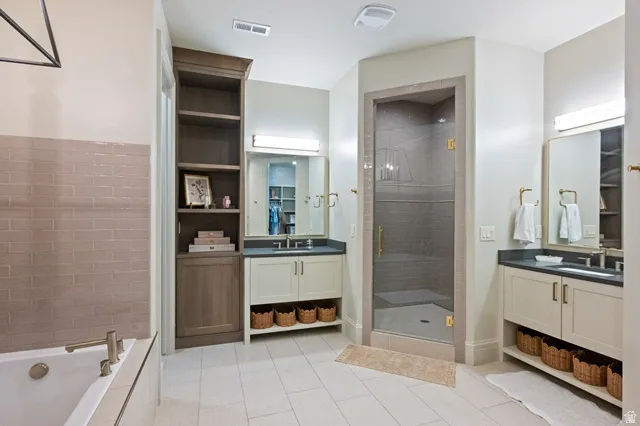 Spacious bathroom featuring a frameless glass shower enclosure, a built-in soaking tub, dual vanities with integrated sinks, custom cabinetry, and large format tile flooring