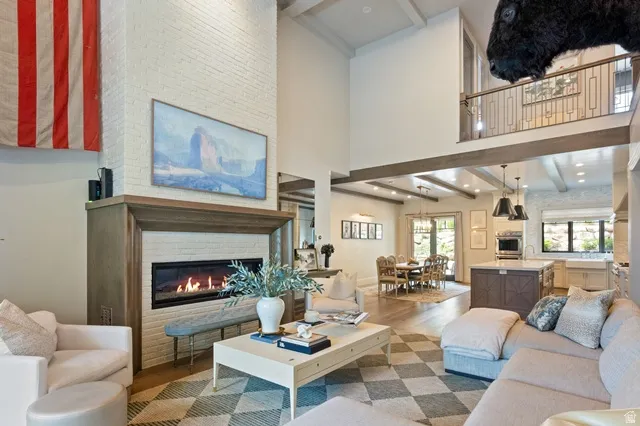 Spacious living area featuring a tall brick fireplace with a wood mantle, high ceilings, and exposed beam accents