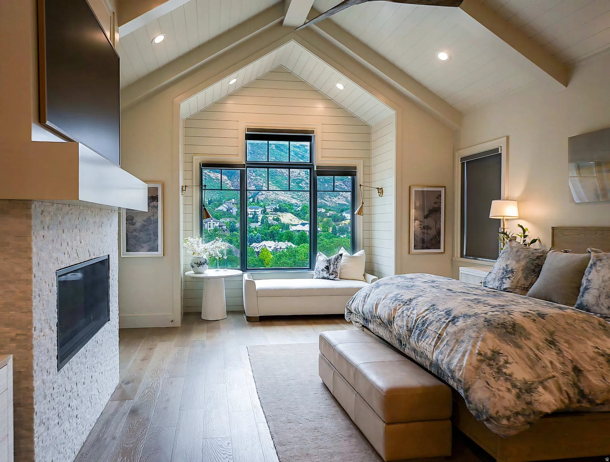 Vaulted ceiling bedroom featuring a floor-to-ceiling window, an integrated window seat, wood-finish flooring, a stone-clad fireplace with a mounted television, and recessed lighting