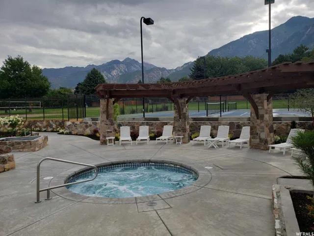 Outdoor spa featuring concrete decking, a stone-clad pergola, and integrated landscaping with mature plantings