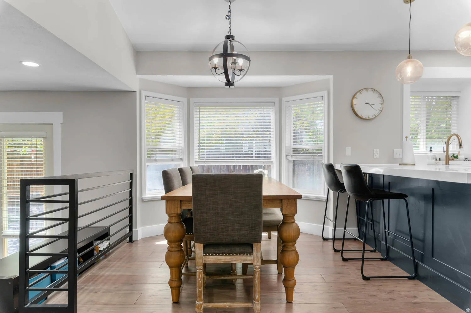Dining area featuring a bay window, wood-finish flooring, a contemporary chandelier, and a metal baluster railing