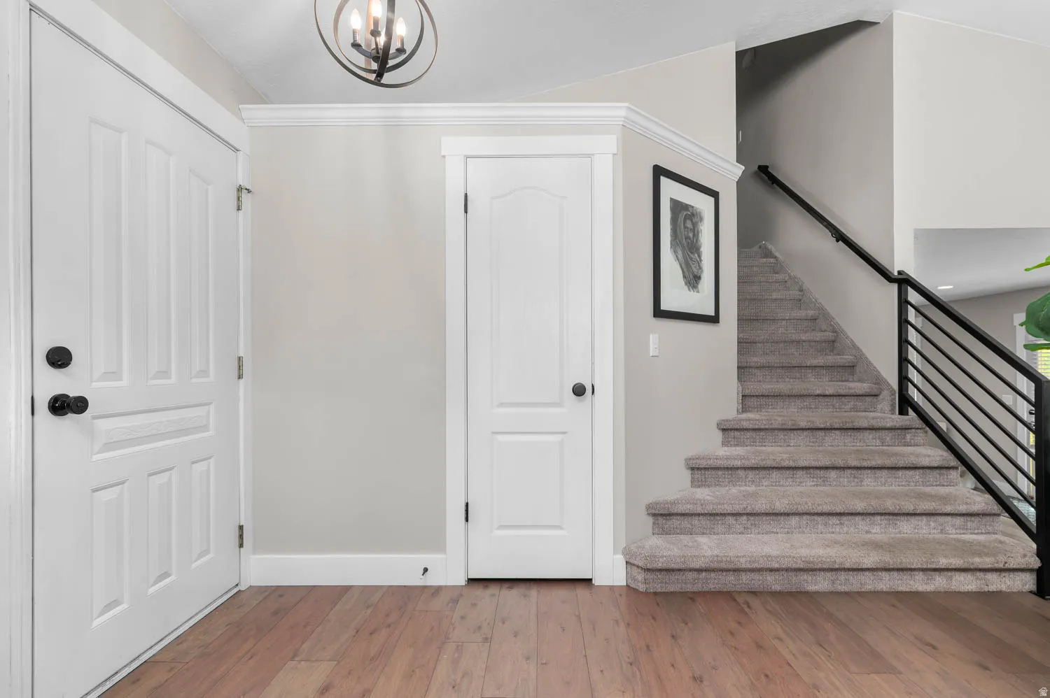 Foyer featuring wood-finish flooring, a contemporary spherical chandelier, white paneled doors with matte black hardware, and a carpeted staircase with a modern black railing
