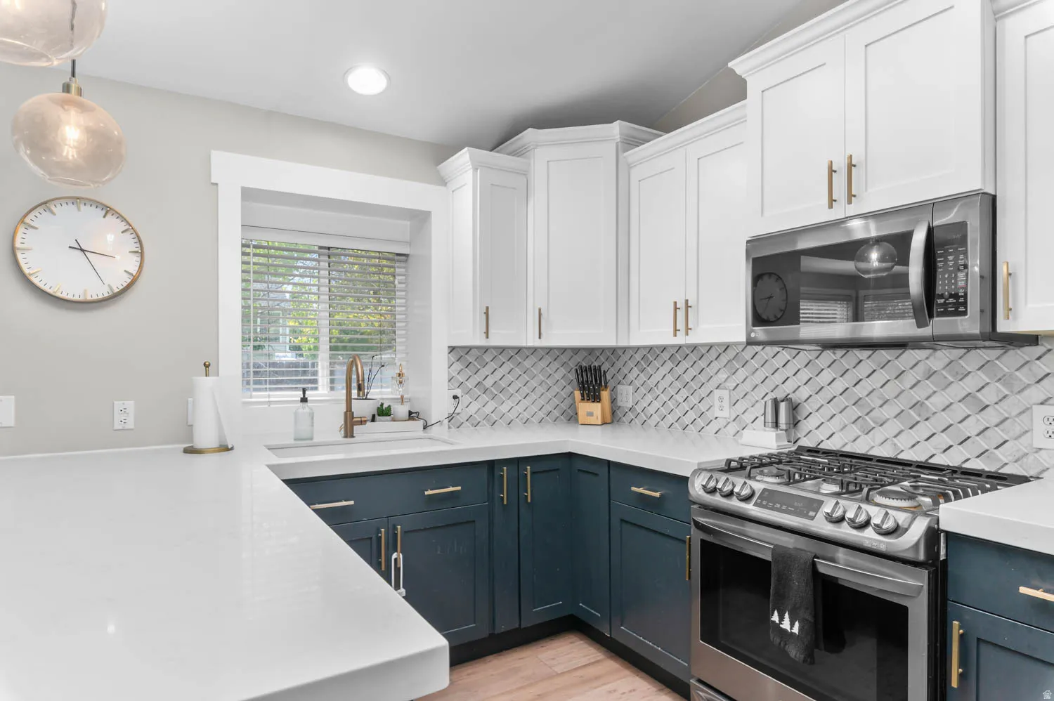 Modern kitchen featuring two-tone cabinetry, stainless steel range with gas burners, white quartz countertops, a window overlooking exterior greenery, and a geometric tile backsplash