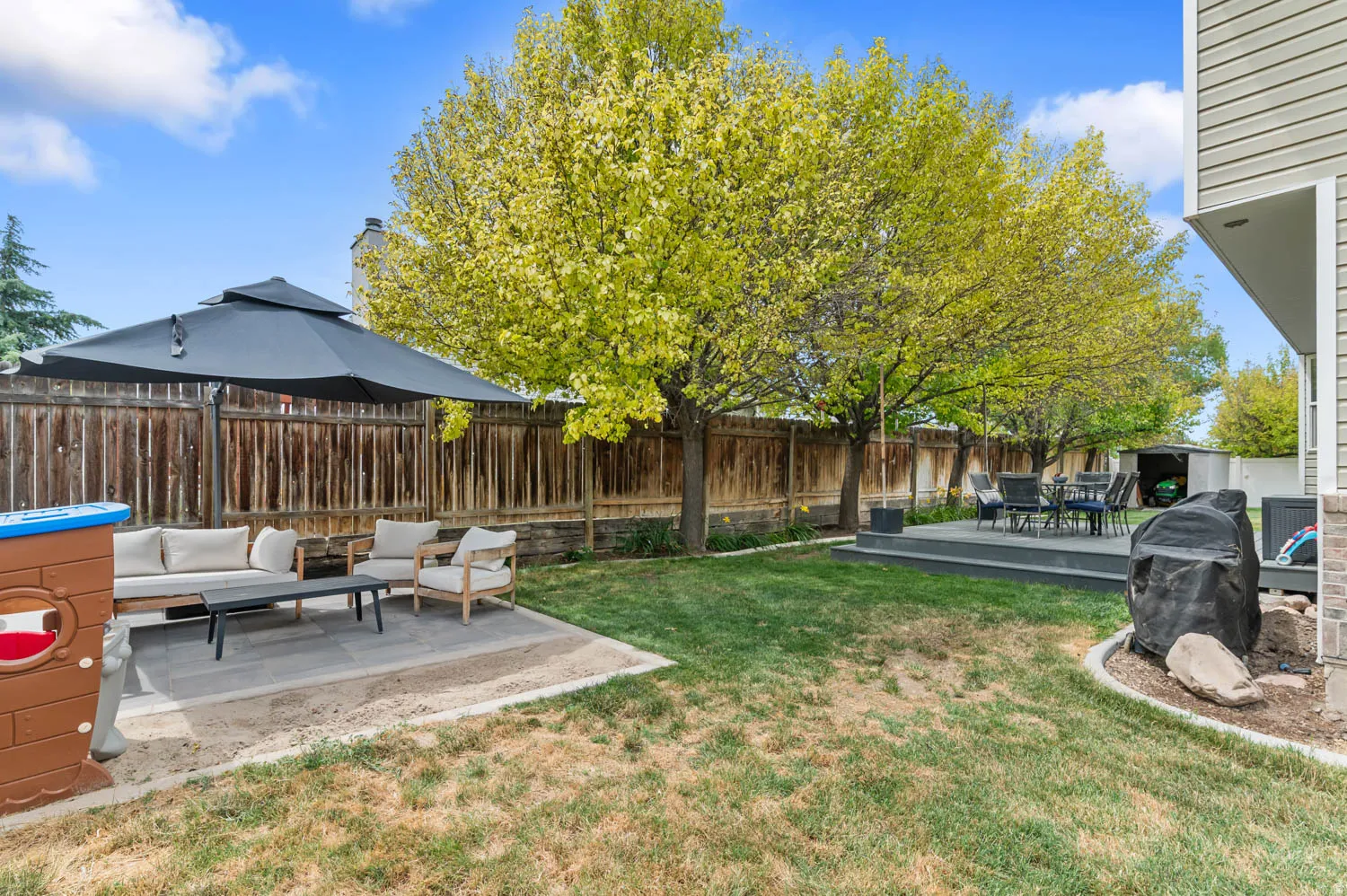 Expansive backyard featuring a manicured lawn, a raised composite deck for outdoor dining, and a stone patio