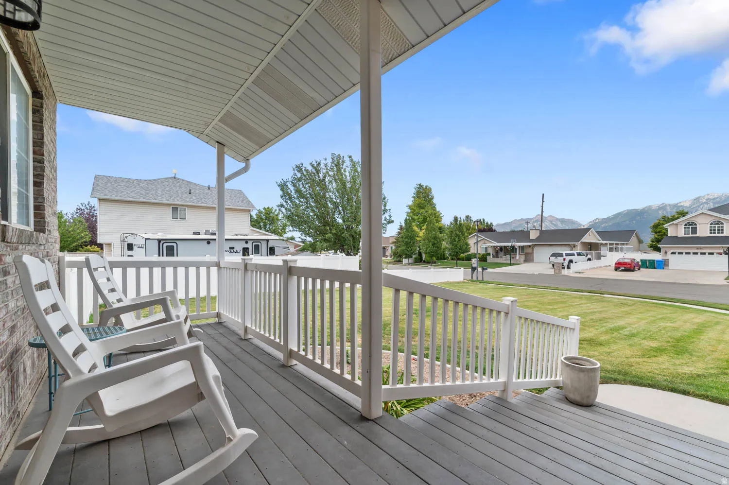 Covered front porch with grey wood-finish decking, white baluster railing, brick exterior, and a white soffit ceiling