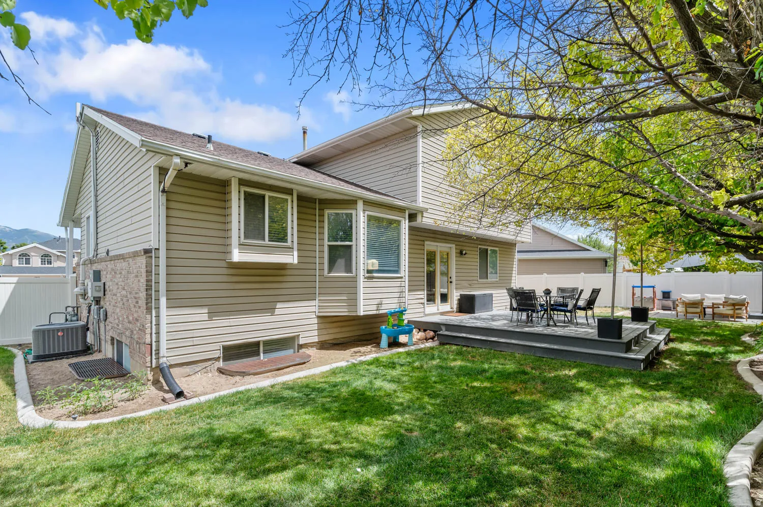 Spacious backyard with a multi-level deck featuring a perimeter railing, surrounded by a manicured lawn and mature trees