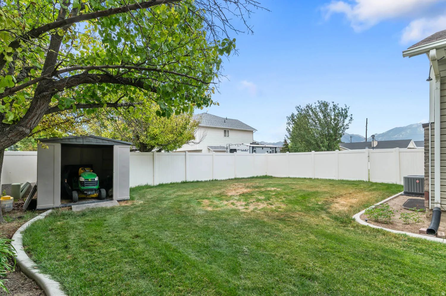Expansive backyard featuring a manicured lawn, a white privacy fence, and a storage shed