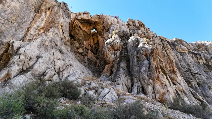 Natural rock formation featuring an archway, rock outcroppings, a rugged stone face, and sparse desert vegetation