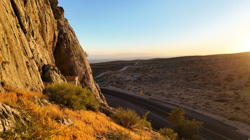 Natural rock formation with stratified cliffs, desert landscape, and an asphalt road