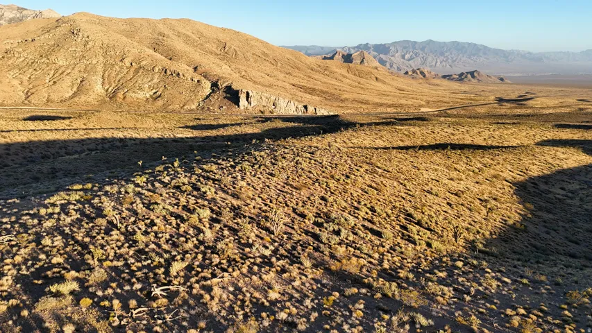 Expansive desert landscape featuring rolling hills, sparse vegetation, and distant mountain ranges under a clear sky