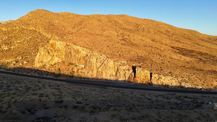 Desert landscape featuring expansive hillsides, rocky outcrops, and a paved road winding through the terrain