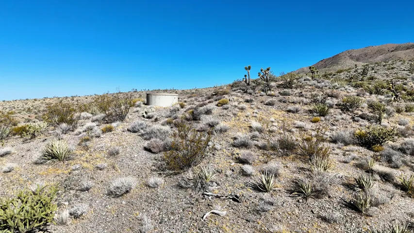 Desert landscape featuring a circular concrete structure, sparse native vegetation, and a clear sky