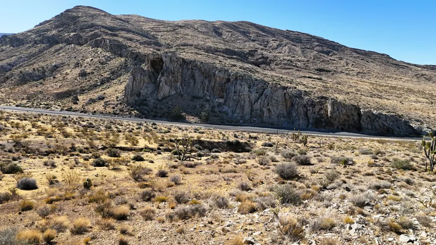 Expansive desert landscape featuring rugged mountain terrain, natural rock formations, and a paved roadway