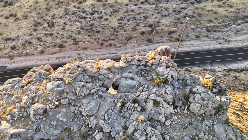 Rocky terrain featuring a two-lane paved road, scattered low-lying vegetation, and varied rock formations