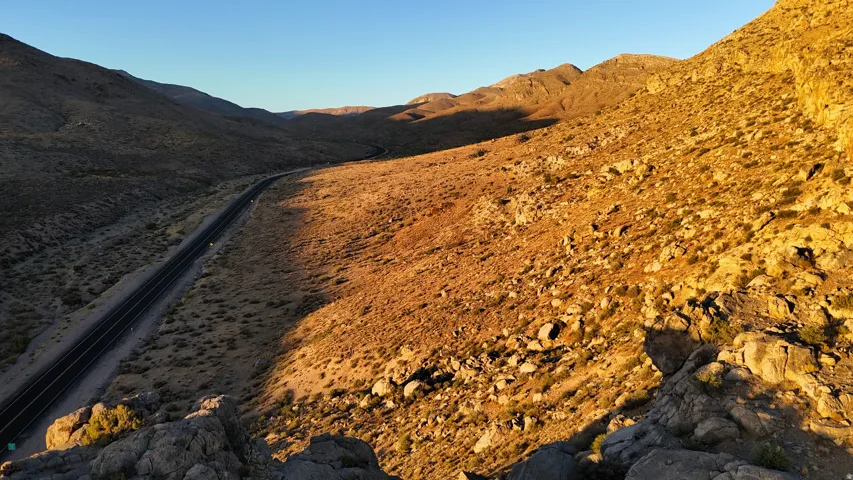 Scenic desert landscape featuring expansive rugged terrain, distant mountains, and a winding paved road