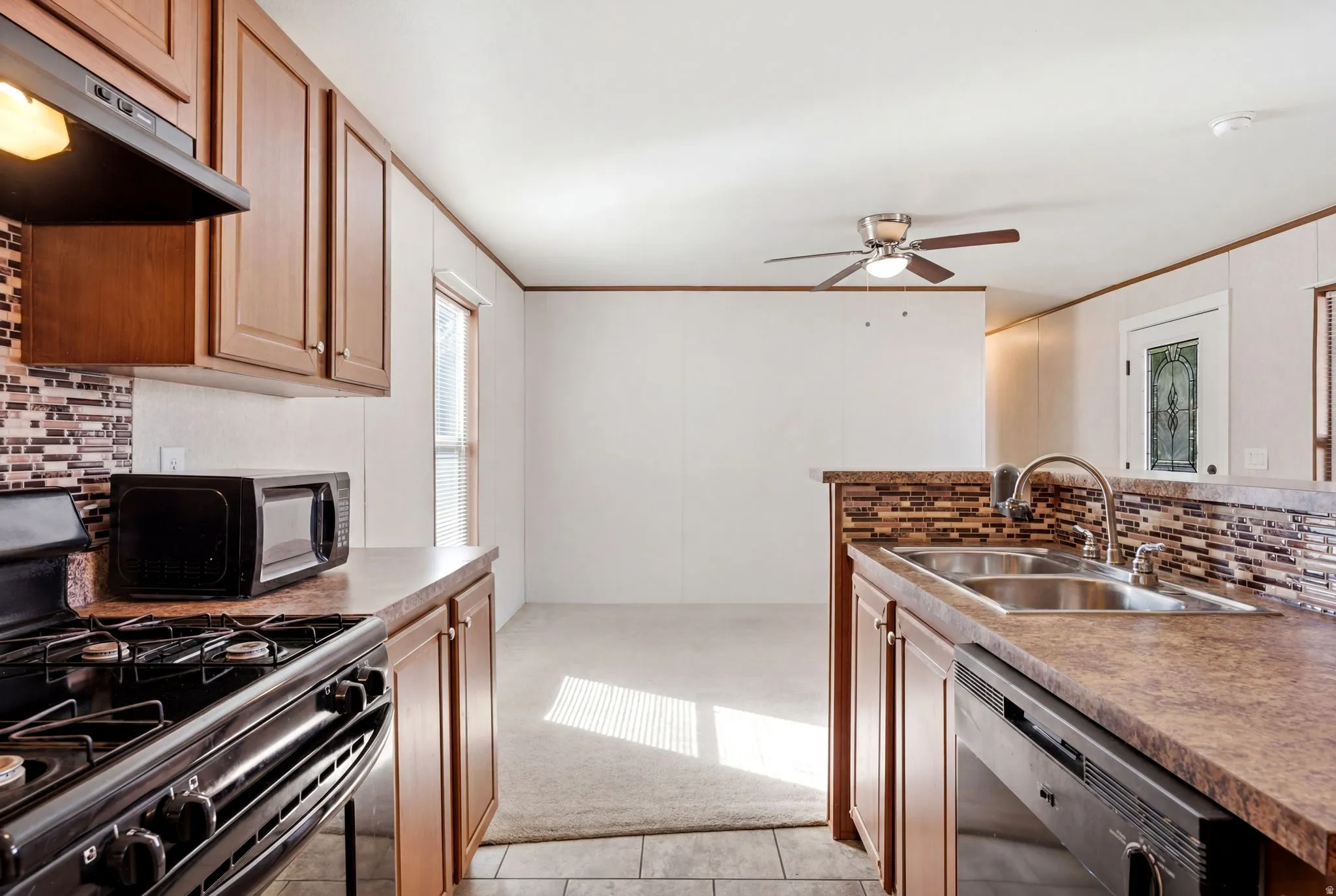 Kitchen featuring wood-finish cabinetry, a mosaic tile backsplash, double basin sink, and a black built-in dishwasher