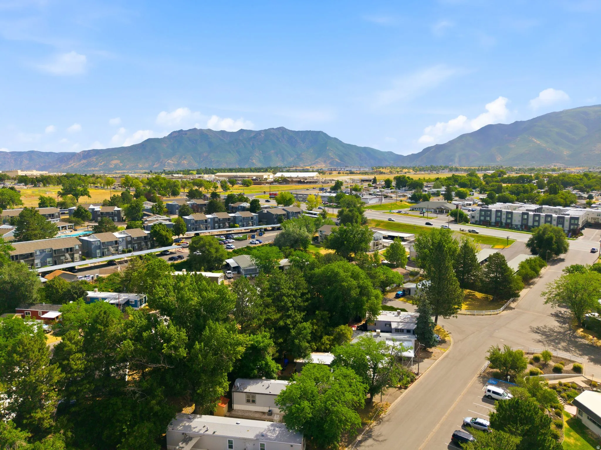 Expansive residential area featuring a mix of housing types, mature trees, paved roads, and distant mountains