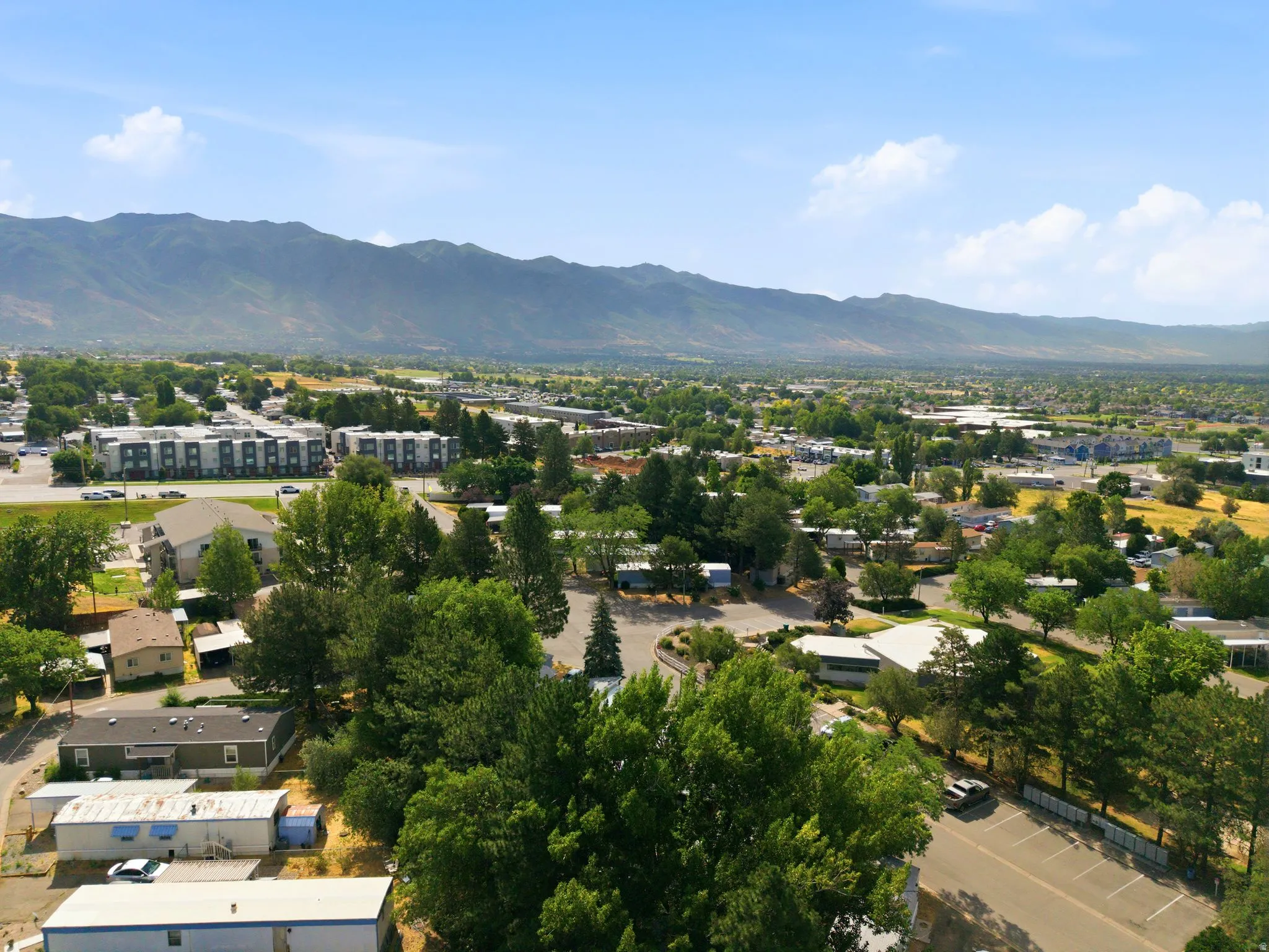 Expansive aerial perspective showcasing a mountainous backdrop, a verdant landscape with mature trees, and a mix of residential and commercial structures