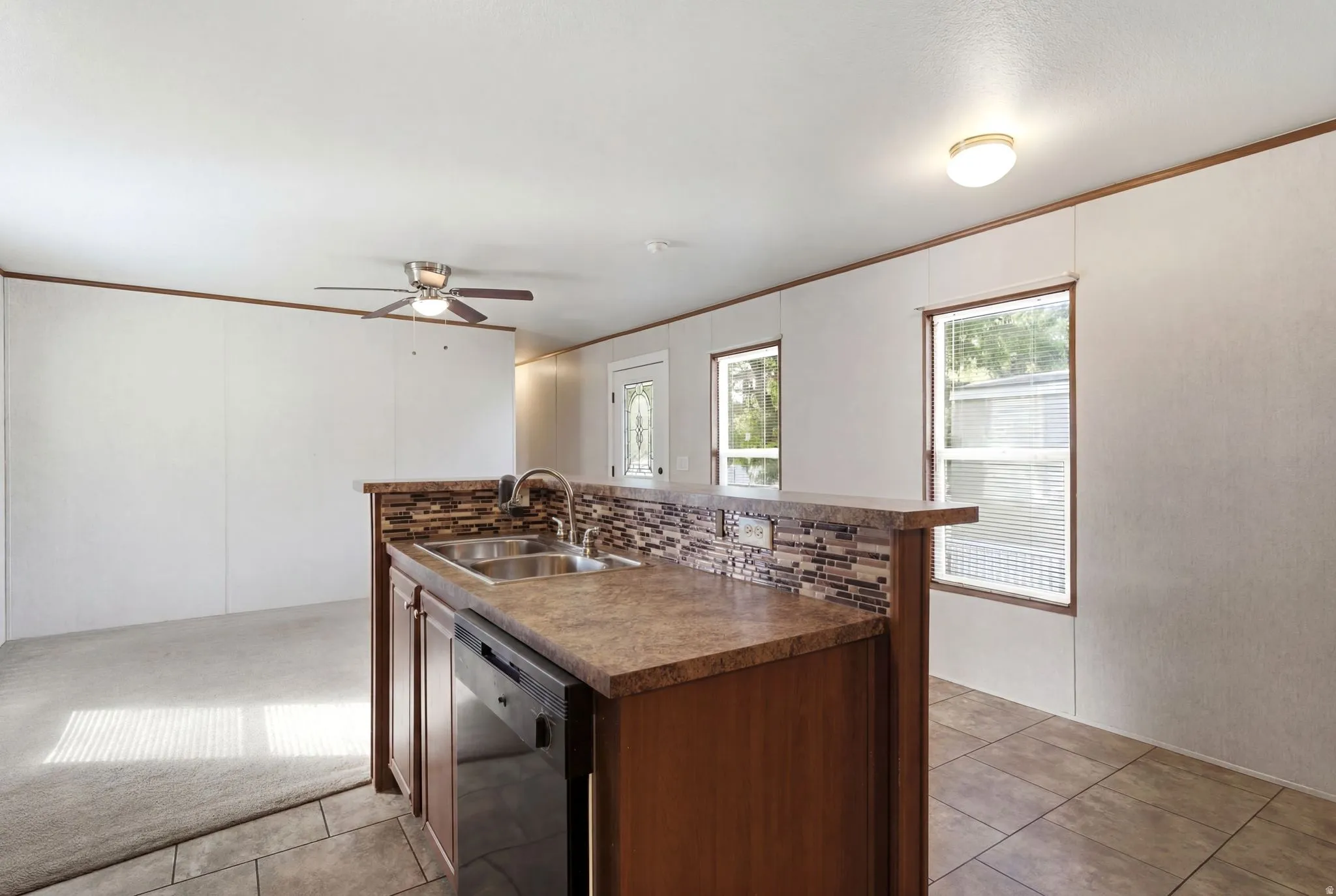 Kitchen island featuring a double-basin stainless steel sink with a high-arc faucet, integrated dishwasher, and a mosaic tile backsplash