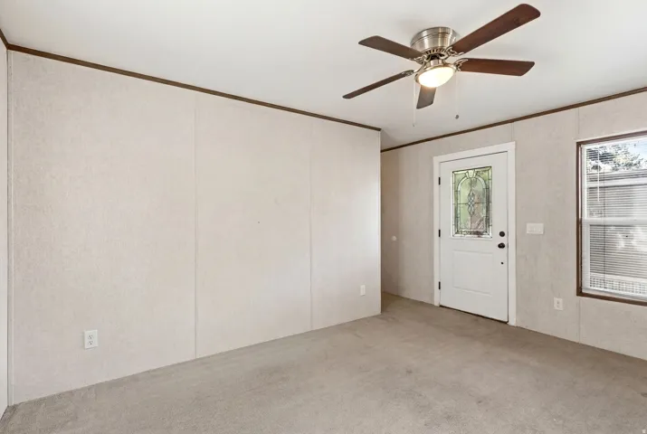 Neutral-toned panel walls with wood trim, featuring a ceiling fan with light fixture, a white door with decorative glass insert, and a window with blinds
