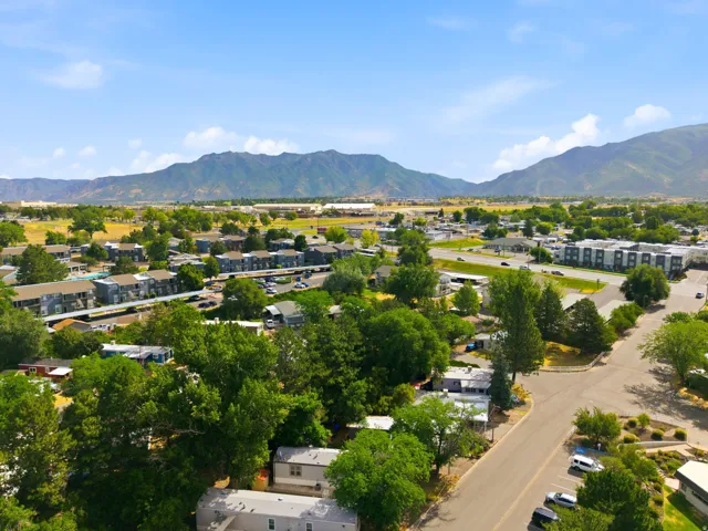 Expansive residential area featuring a mix of housing types, mature trees, paved roads, and distant mountains