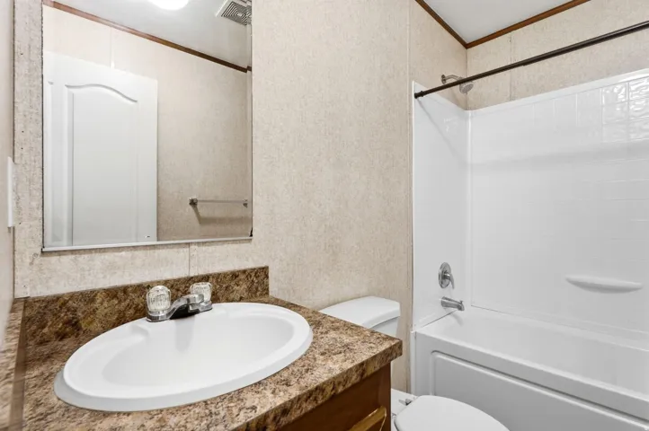 Bathroom featuring a white drop-in sink, a speckled countertop, and a white tub with an integrated shower