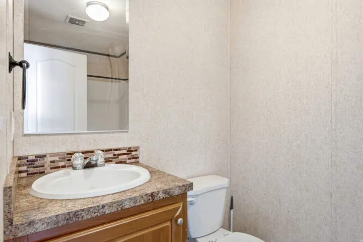Bathroom vanity featuring a white oval sink, chrome faucet, and a brown patterned countertop with a mosaic tile backsplash