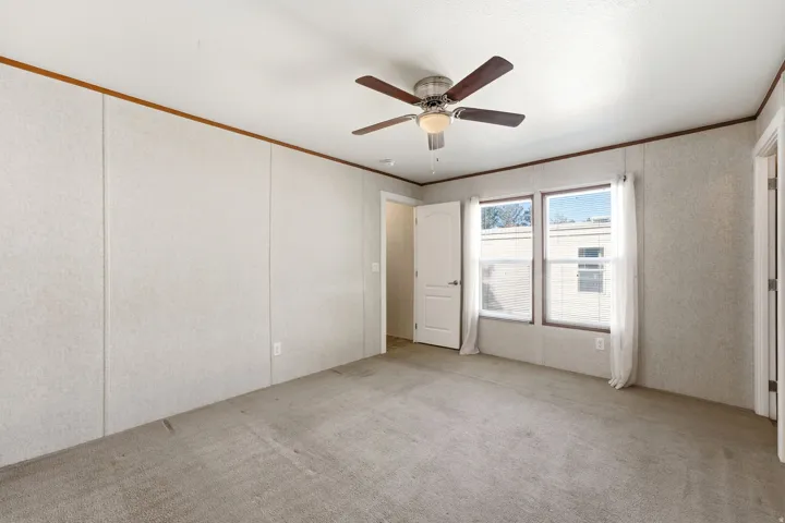Spacious room featuring neutral carpeting, light-toned wall paneling, and a ceiling fan with integrated lighting