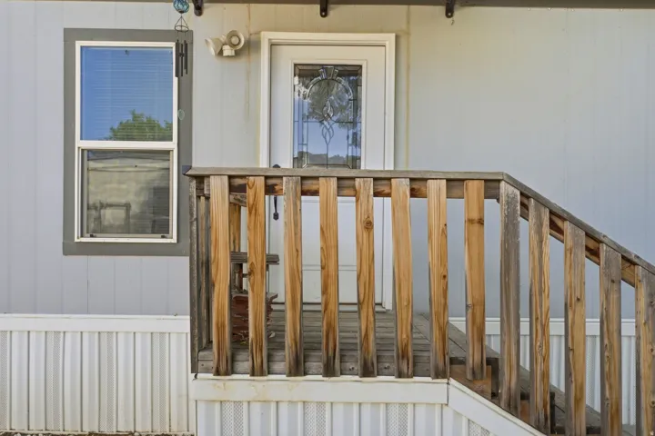 Front entry featuring wood-plank railing and steps, a white paneled door with decorative glass inlay, and light gray vertical siding
