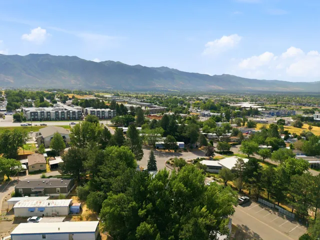 Expansive aerial perspective showcasing a mountainous backdrop, a verdant landscape with mature trees, and a mix of residential and commercial structures