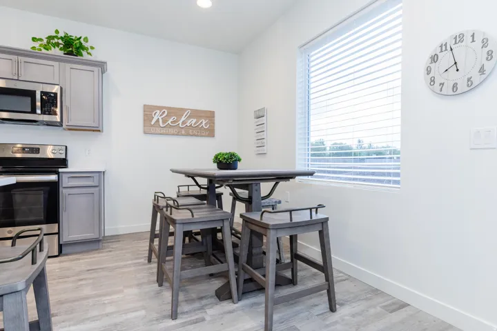 Kitchen and dining area featuring light gray cabinetry, stainless steel appliances, a white countertop, wood-finish flooring, and a large window with blinds
