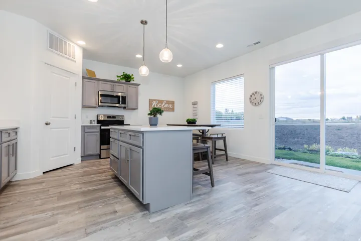 Kitchen featuring a central island with countertop seating, stainless steel appliances, grey cabinetry, and wood-finish flooring