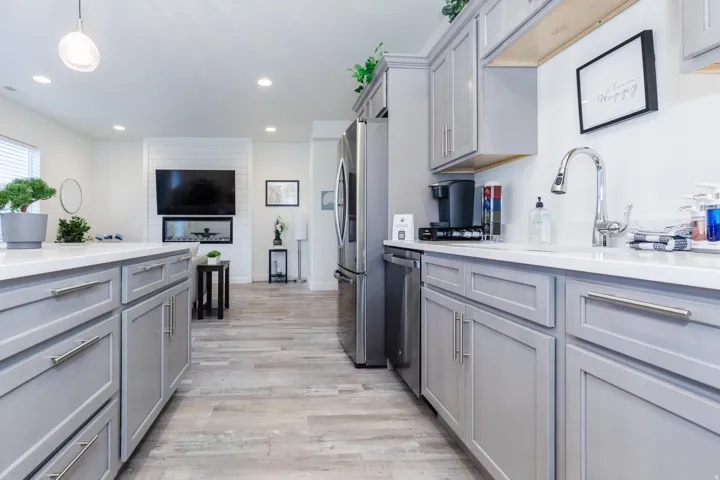 Open-concept kitchen featuring light gray cabinetry, polished chrome hardware, and white countertops