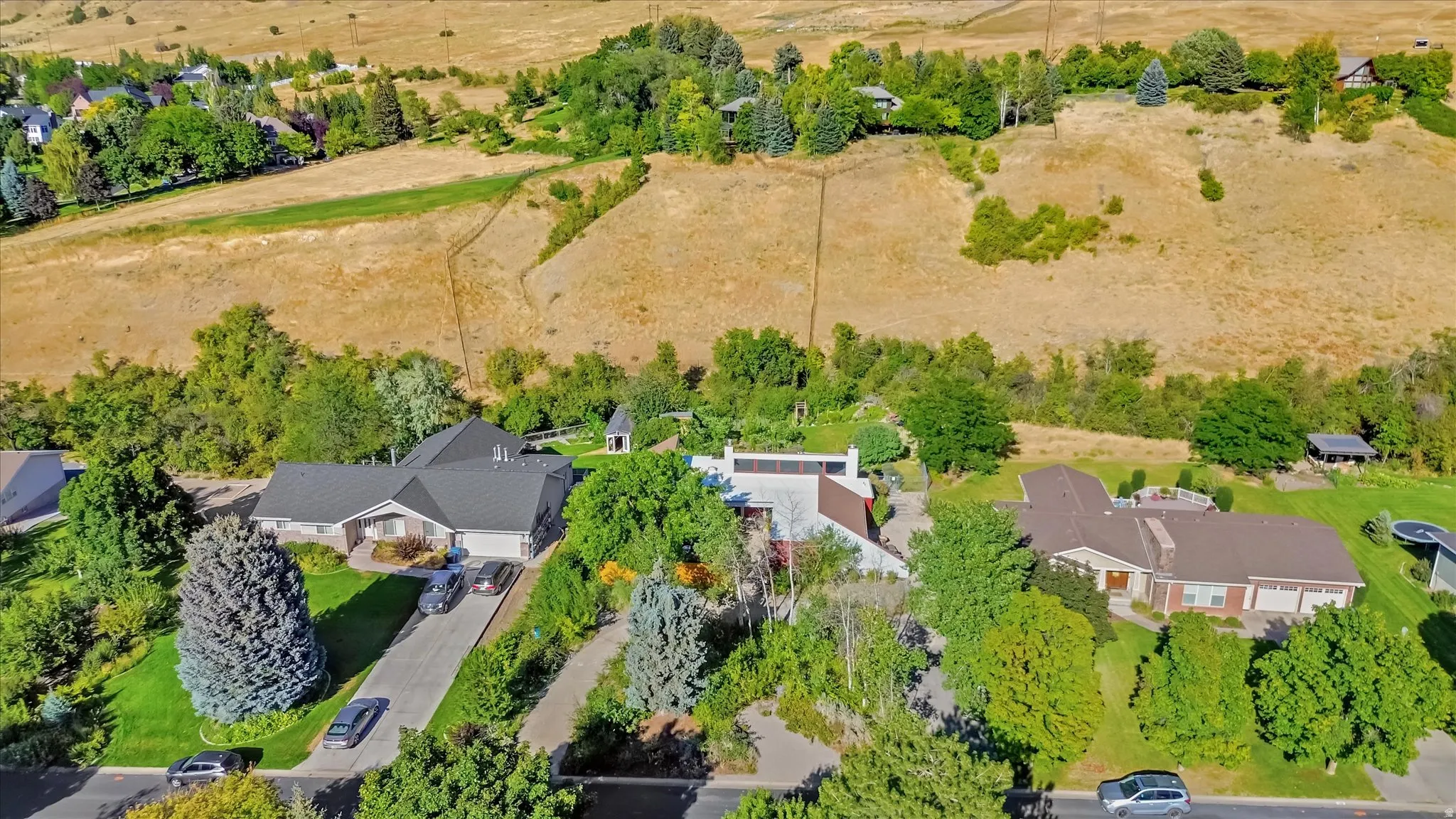 Ranch-style residence featuring a dark shingle roof, attached garage, and a manicured front lawn with mature trees