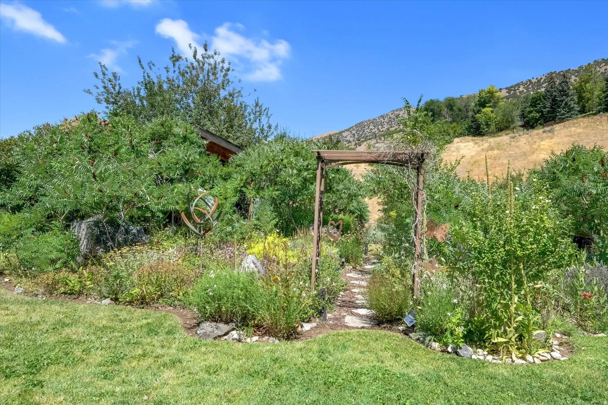 Garden pathway with stone steps and a wooden archway, surrounded by diverse plantings
