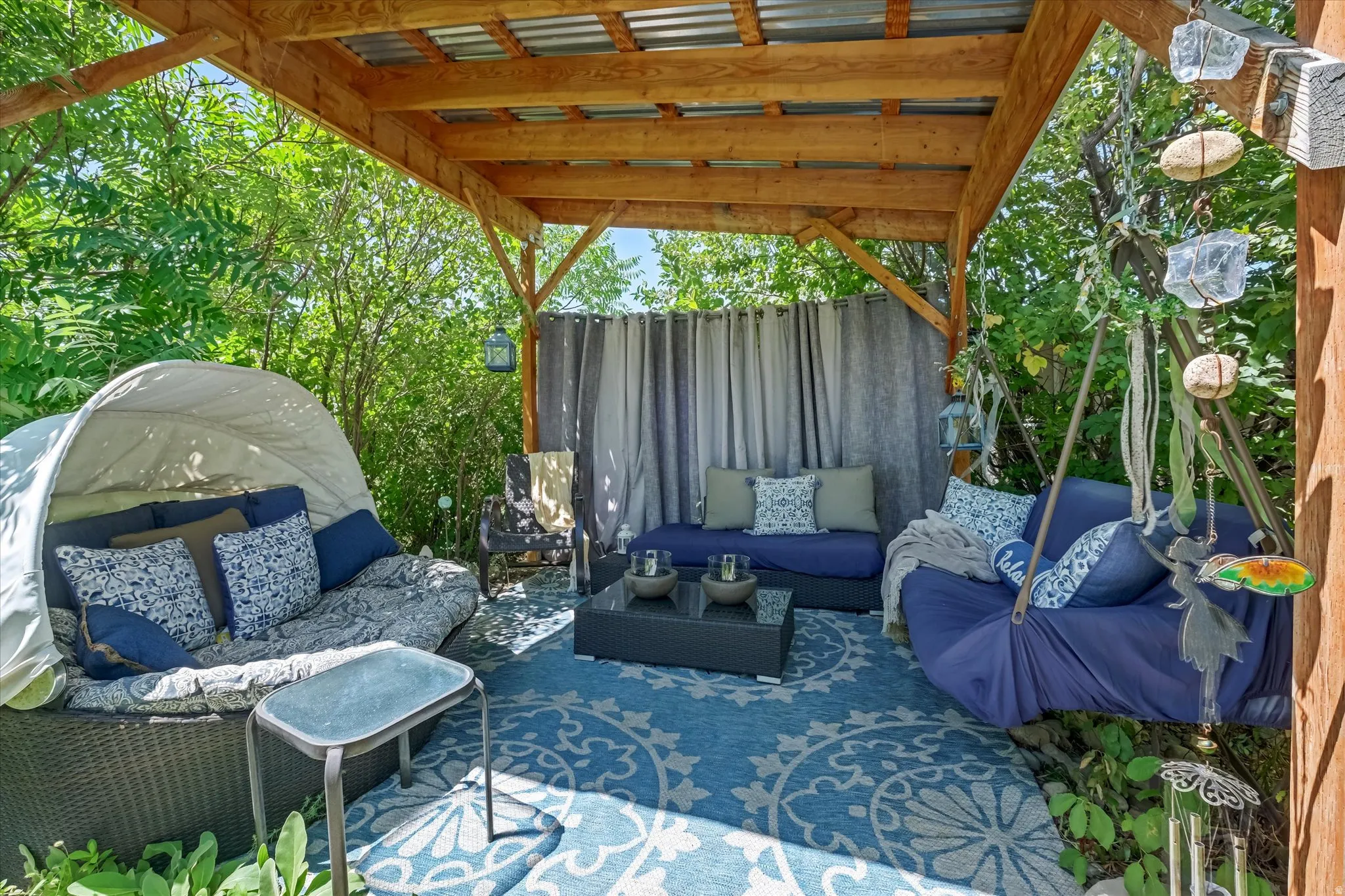 Outdoor wooden pergola featuring a corrugated metal roof, privacy curtains, and a patterned area rug