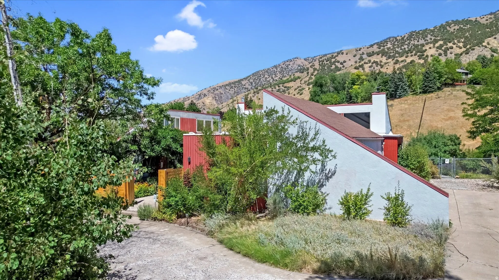 Modern architectural design featuring a red and white exterior, a sloped roofline, a visible chimney, and mature landscaping