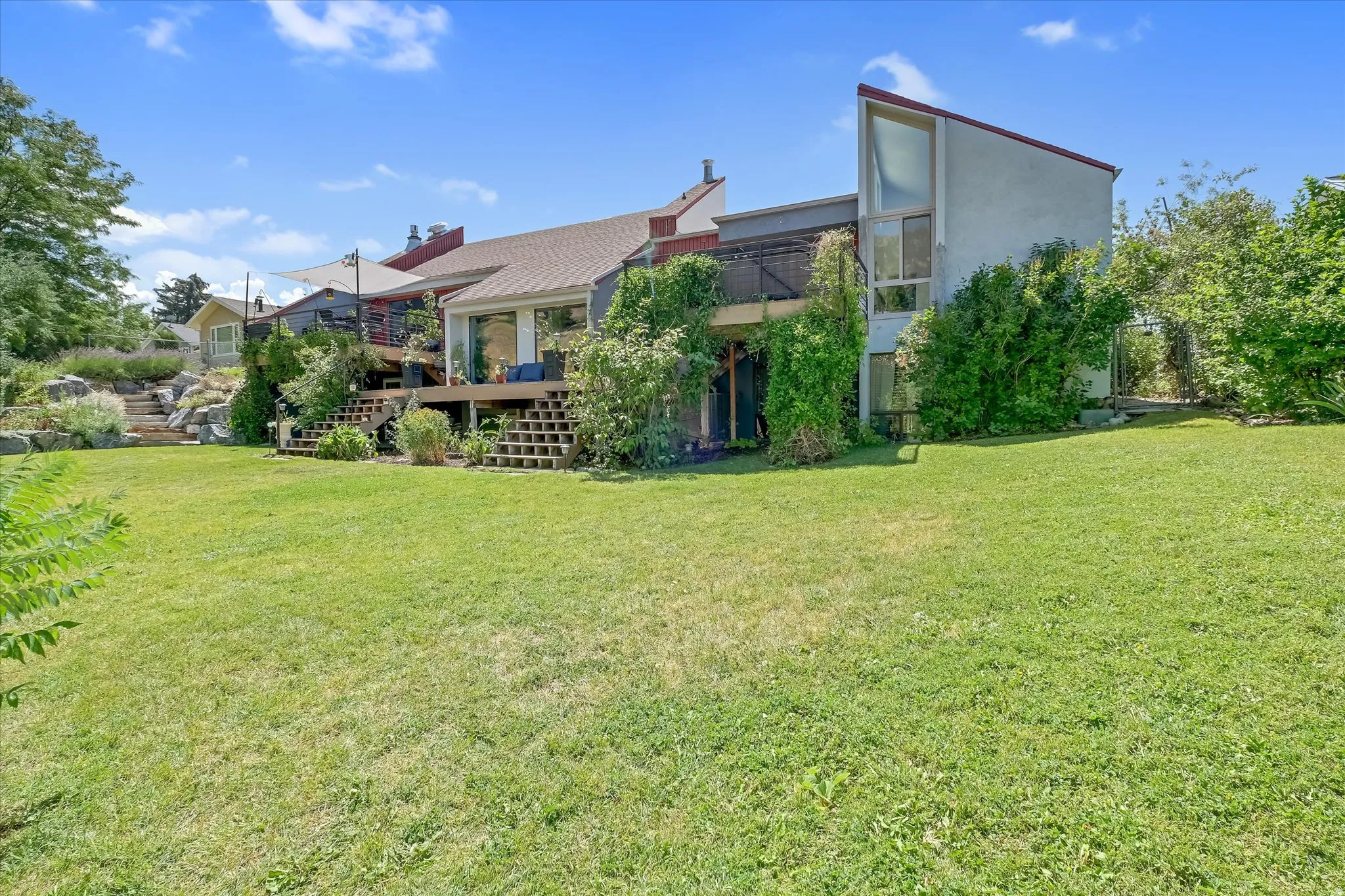 Expansive rear lawn with a multi-level wooden deck featuring a white shade sail