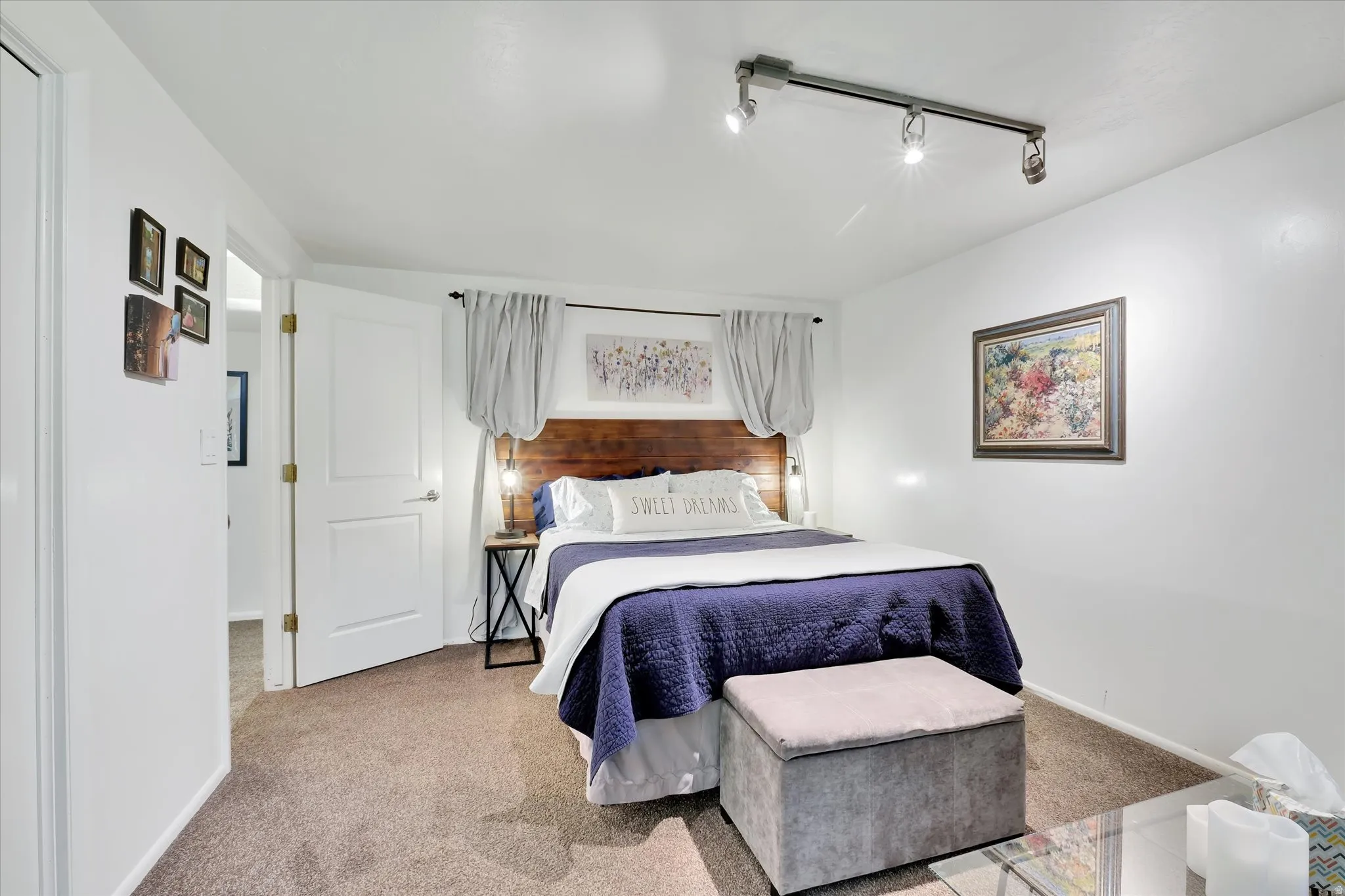 Carpeted bedroom with a built-in wood headboard, white walls, and track lighting