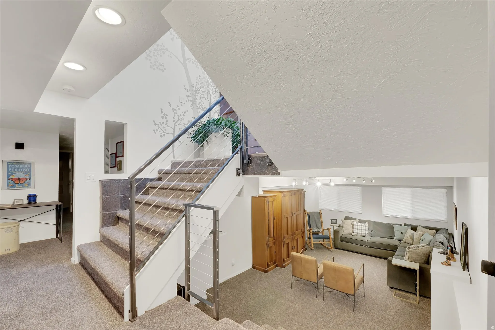 Multi-level interior featuring carpeted stairs with cable railings, recessed lighting, and a lower-level living area with windows