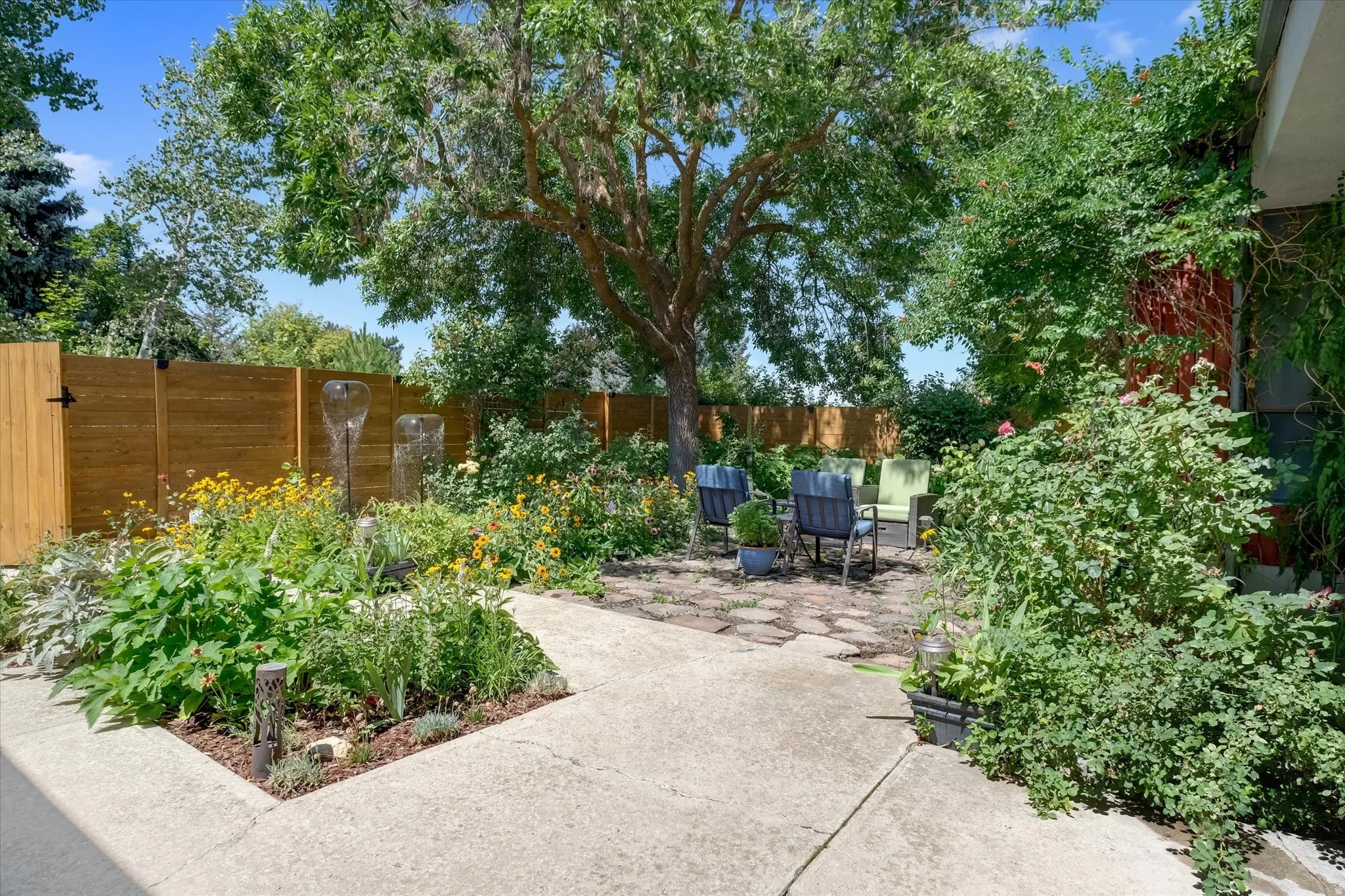 Landscaped backyard featuring a mature tree, stone patio, and perimeter fencing