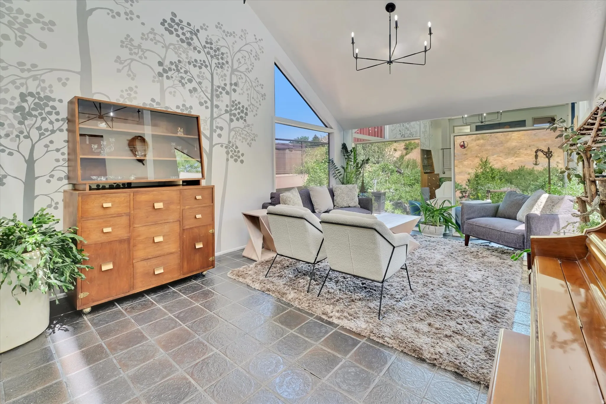 Sun-filled interior space featuring high vaulted ceilings, large picture windows, and dark square tile flooring