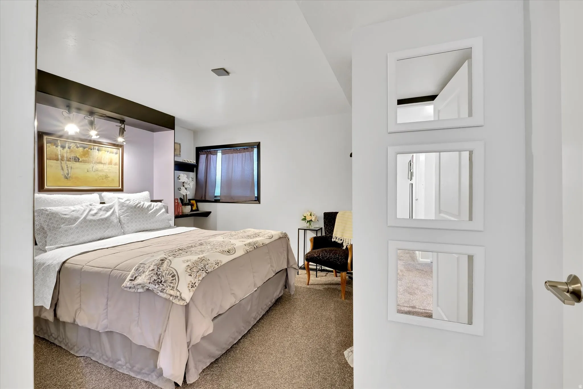 Carpeted bedroom featuring a built-in headboard with integrated shelving and task lighting, a recessed window, and wall-mounted floating shelving
